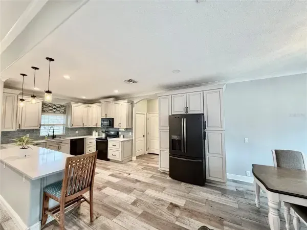 Bright modern kitchen and dining area with white cabinets, black fridge, and light wood floors