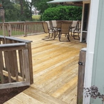 Wooden backyard deck with patio table and chairs, railing, and greenery beyond