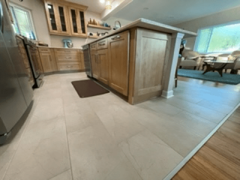 Modern kitchen with light wood cabinets, tiled floor, island, and dining area in the background