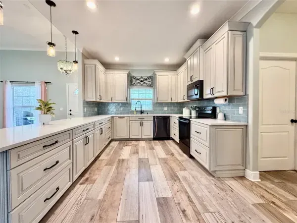 Bright modern kitchen with white cabinets, stainless appliances, and wood-look flooring