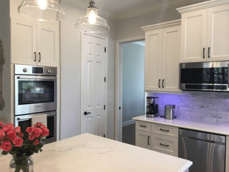 Modern white kitchen with stainless steel appliances, marble island, and pendant lights