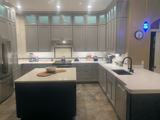 Modern kitchen with gray cabinets, island, white countertops, and blue accent lighting above the sink.