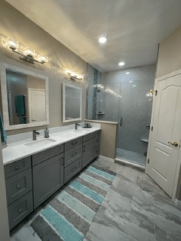 Modern bathroom with double vanity, glass shower, and blue-striped rug