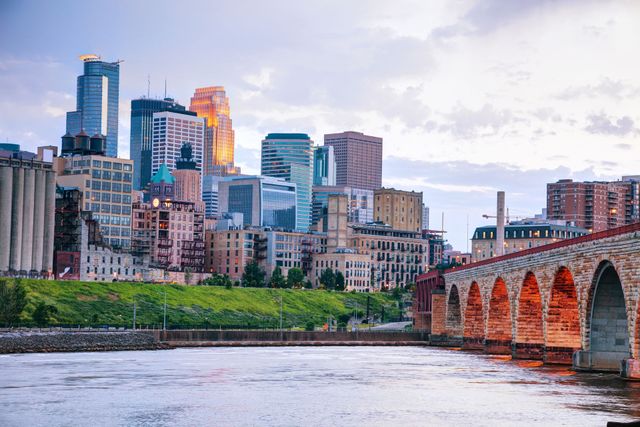 City skyline beside a river with a stone bridge and cloudy sky at dusk