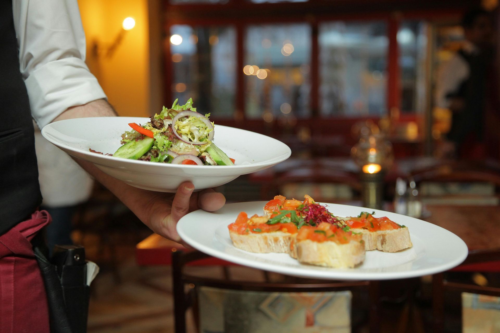 Waiter holding two plates: a salad and bruschetta, in a restaurant.