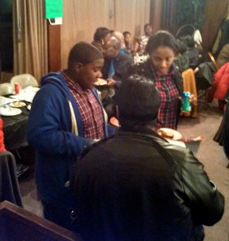 A group of people are gathered in a room with a green sign on the wall