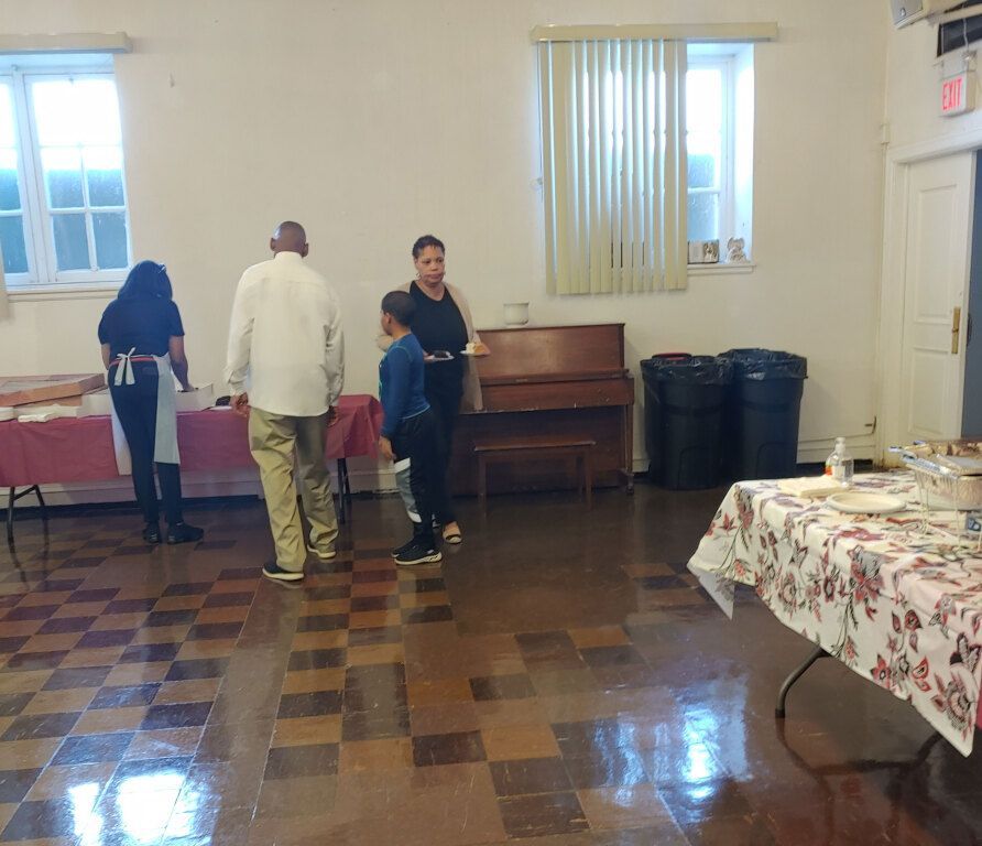 A group of people are standing in a room with tables and a piano.