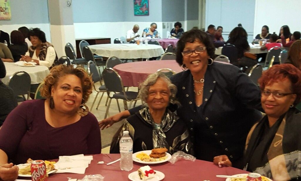 A group of women are posing for a picture while sitting at a table with food.