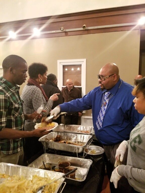 A man in a blue shirt and tie is serving food to a group of people.