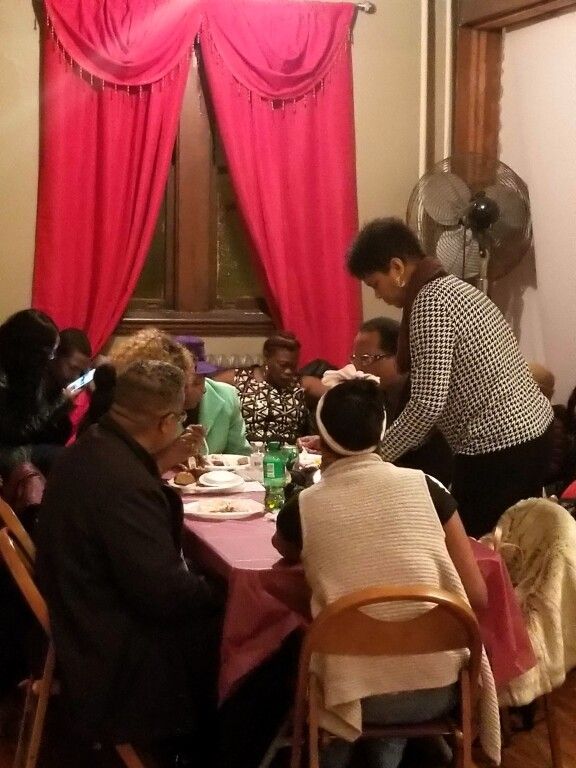 A group of people are sitting at tables in a room with red curtains