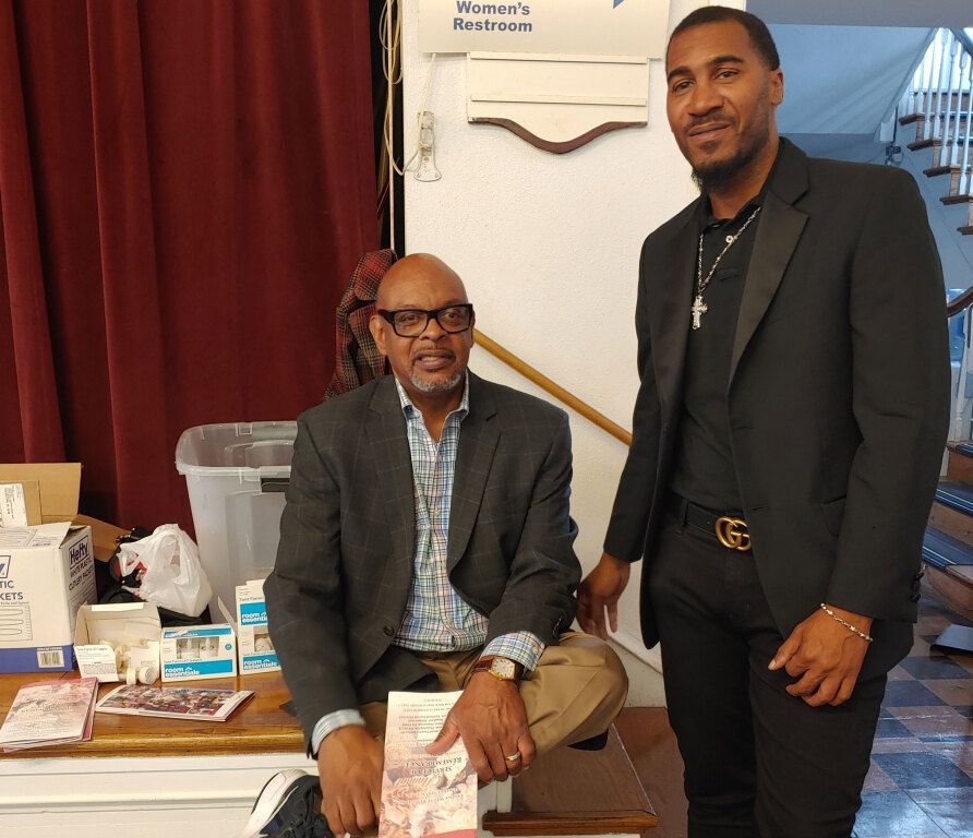 Two men are standing next to each other and one is holding a book