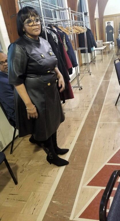 A woman in a black leather dress is standing in a room.