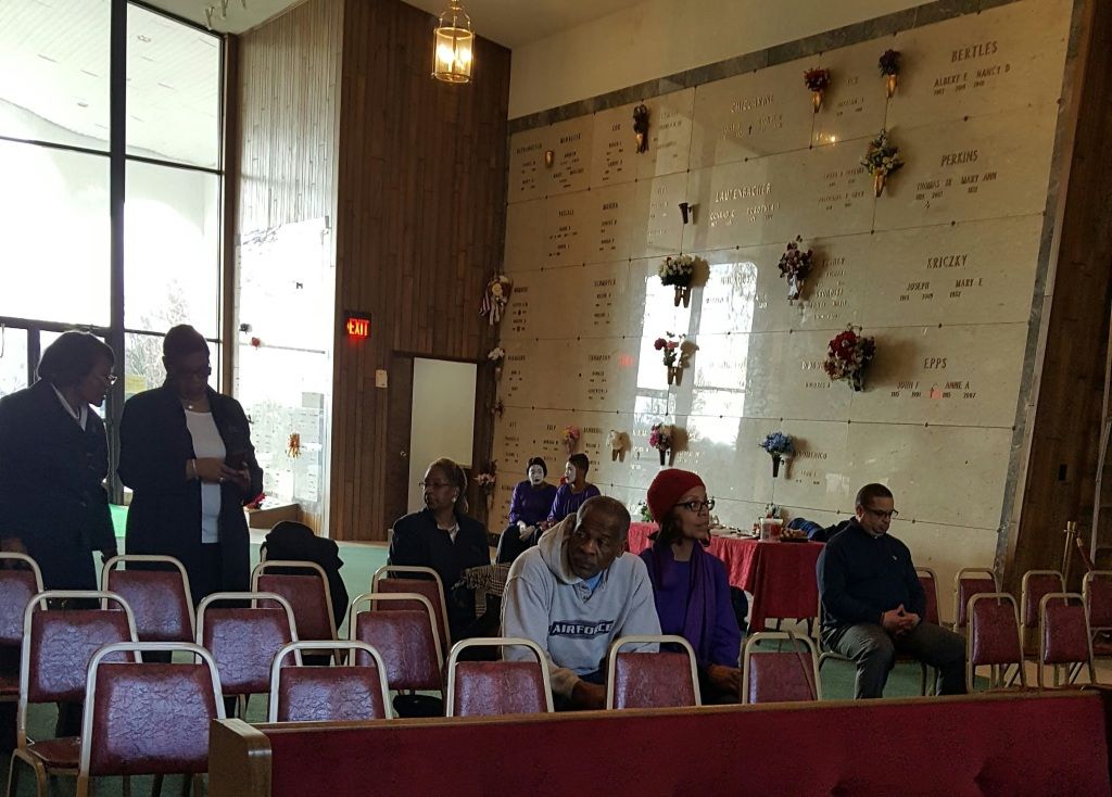 A group of people are sitting in a room in front of a wall with flowers on it.