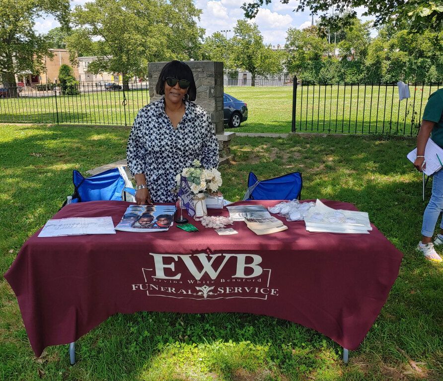 A woman is standing in front of a table that says ewb funeral service