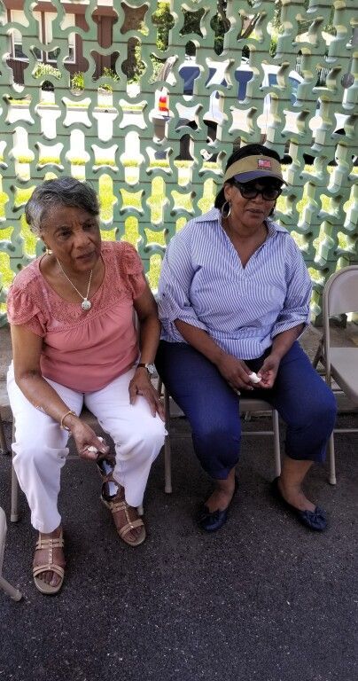 Two women are sitting in chairs in front of a green wall