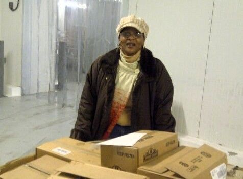 A woman in a brown jacket is sitting in front of a pile of boxes