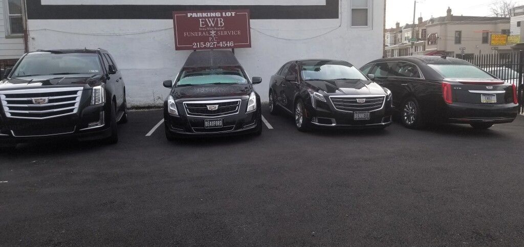 A row of cars are parked in a parking lot in front of a building.