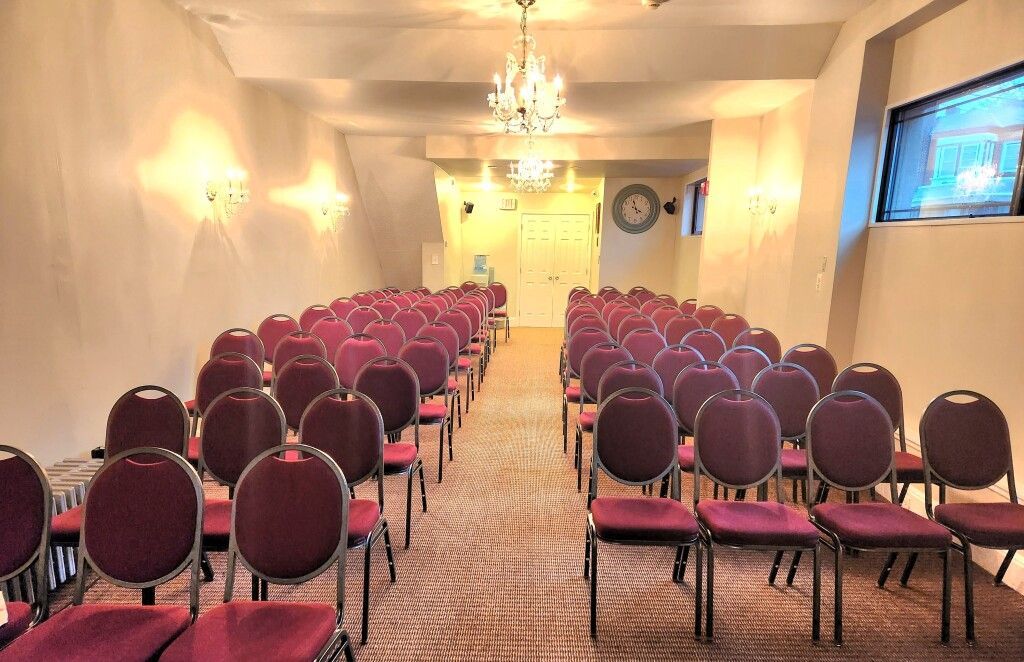 A room filled with rows of red chairs and a chandelier.
