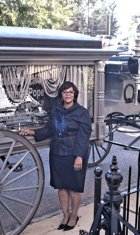 A woman is standing in front of a horse drawn carriage.