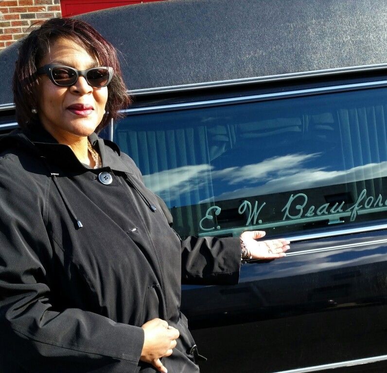 A woman wearing sunglasses stands in front of a black limousine that says e. w. beaufor