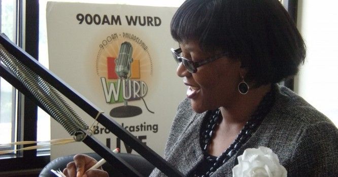A woman is sitting in front of a sign that says 900am wurd