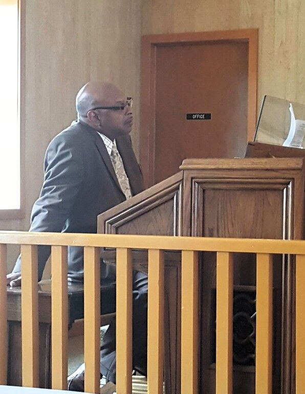 A man in a suit and tie is sitting at a podium in a courtroom