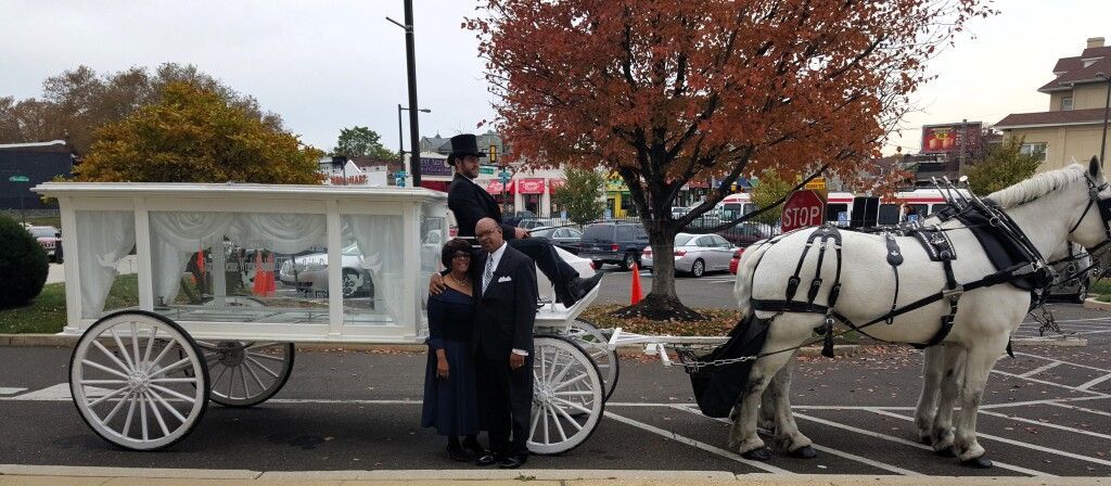 A horse drawn carriage in a parking lot with people standing in front of it