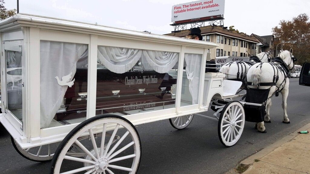 A horse drawn carriage with a coffin in it is parked on the side of the road.