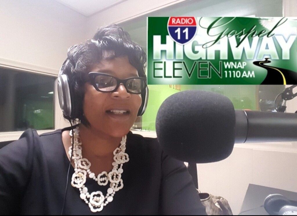 A woman wearing headphones and a necklace is sitting in front of a microphone for radio 11 highway eleven