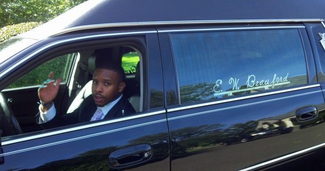 A man is sitting in the driver 's seat of a black limousine.