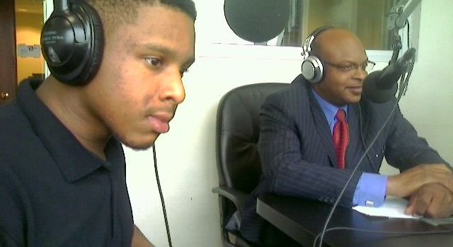 A man wearing headphones is talking to another man in a suit