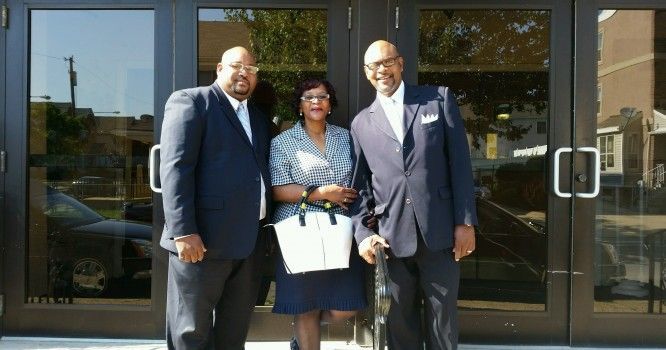 Two men and a woman are posing for a picture in front of a building.