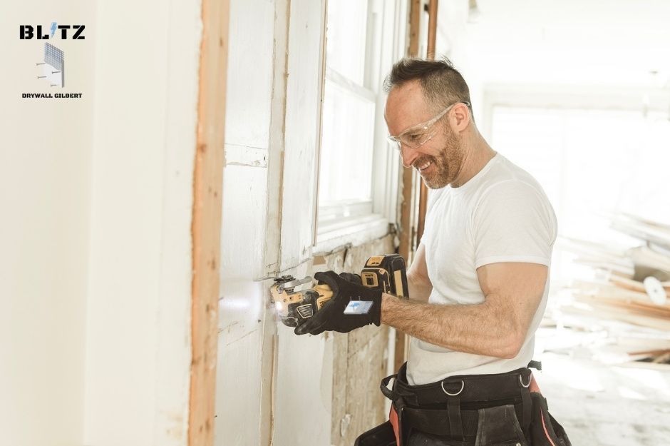 A drywall repair handyman wearing safety glasses and black gloves uses a oscillating tool on a residential renovation project. He is dressed in a white shirt with a tool belt, working on drywall cutting in a home near W El Sueno Ct, and N Montecito Ave in Sun City West, AZ.