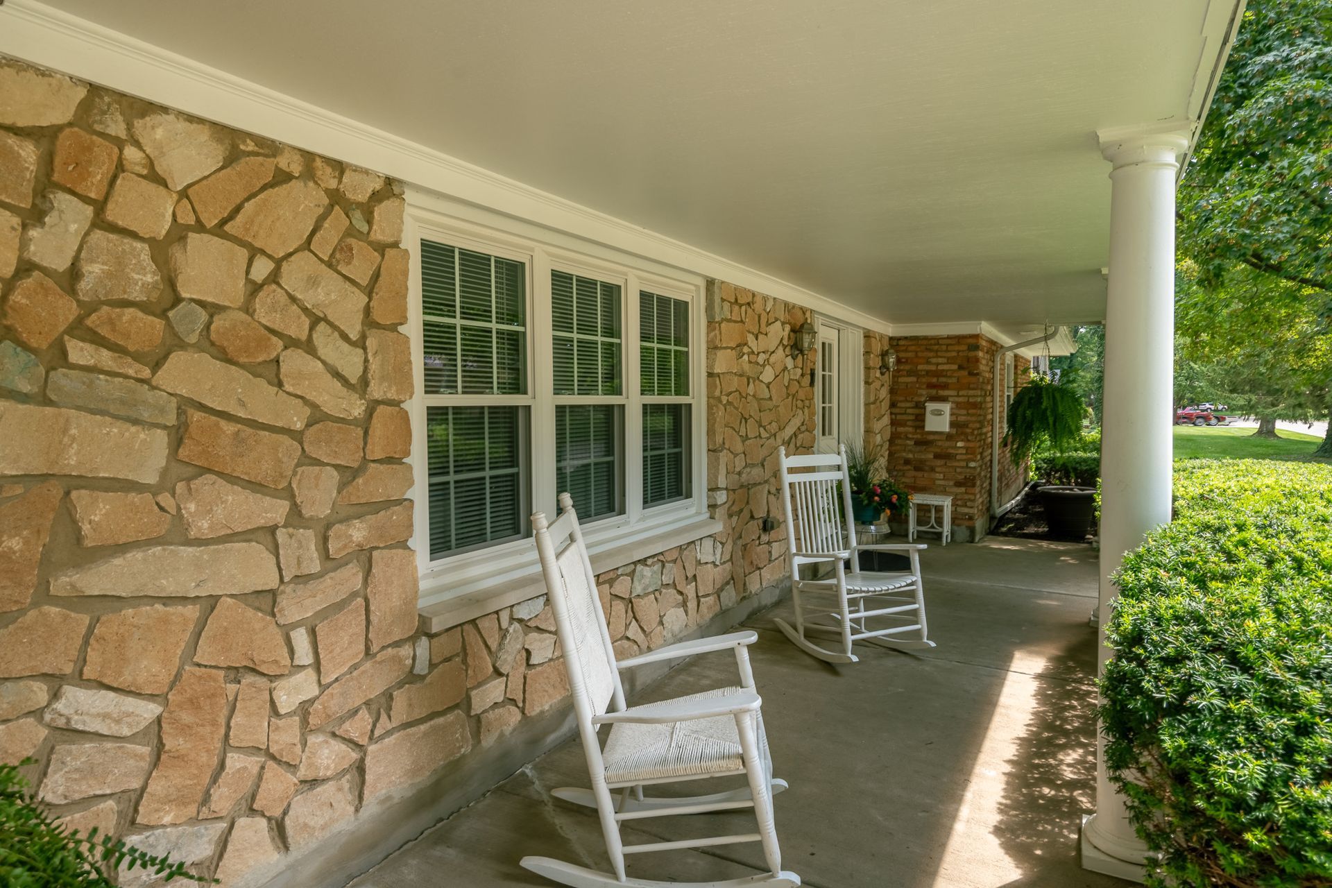 Covered porch with stone wall, white rocking chairs, and shuttered windows.