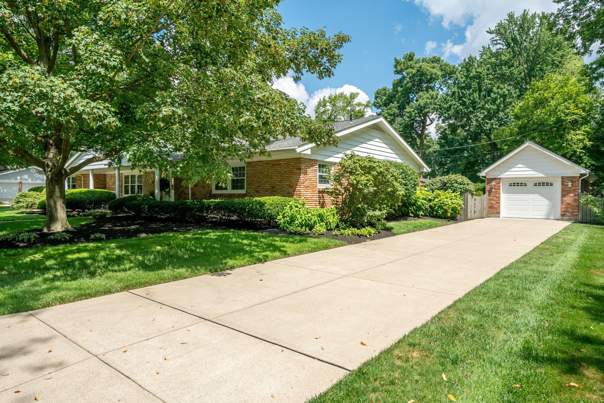 Ranch-style house with attached garage, long driveway, and well-manicured lawn under a sunny sky.
