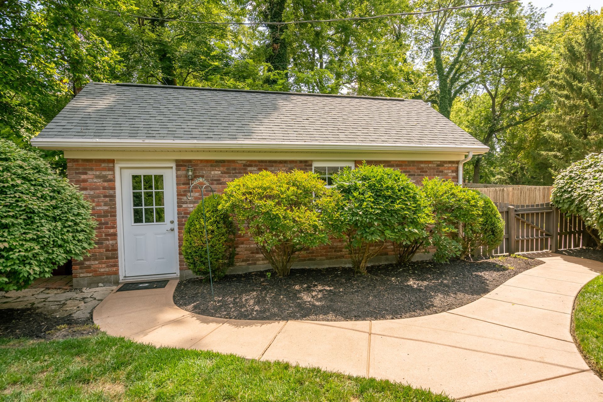 Brick building with white door, bushes, and a curved walkway. Green grass surrounds.