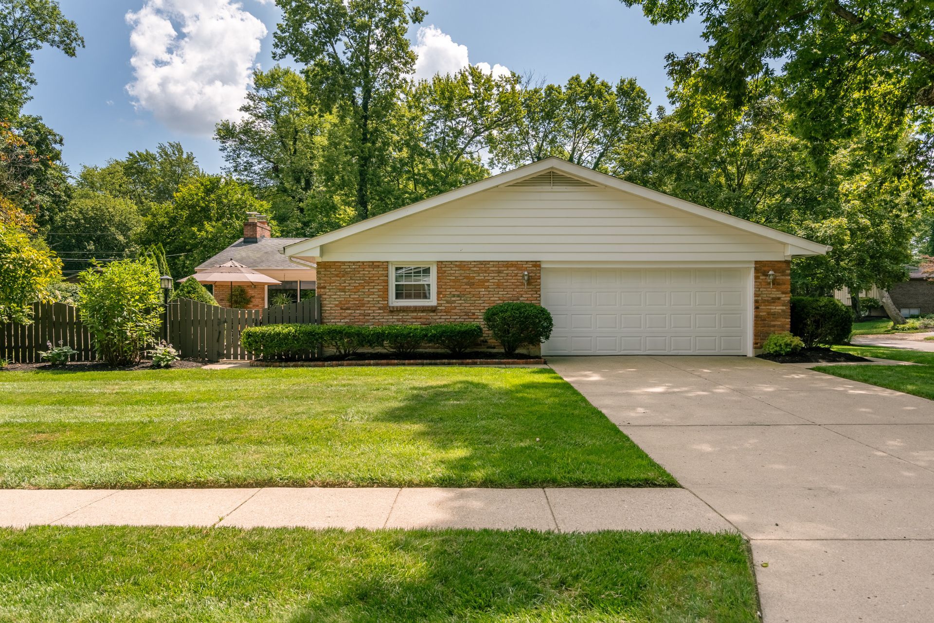 A one-story brick and siding house with a two-car garage, on a green lawn with trees.