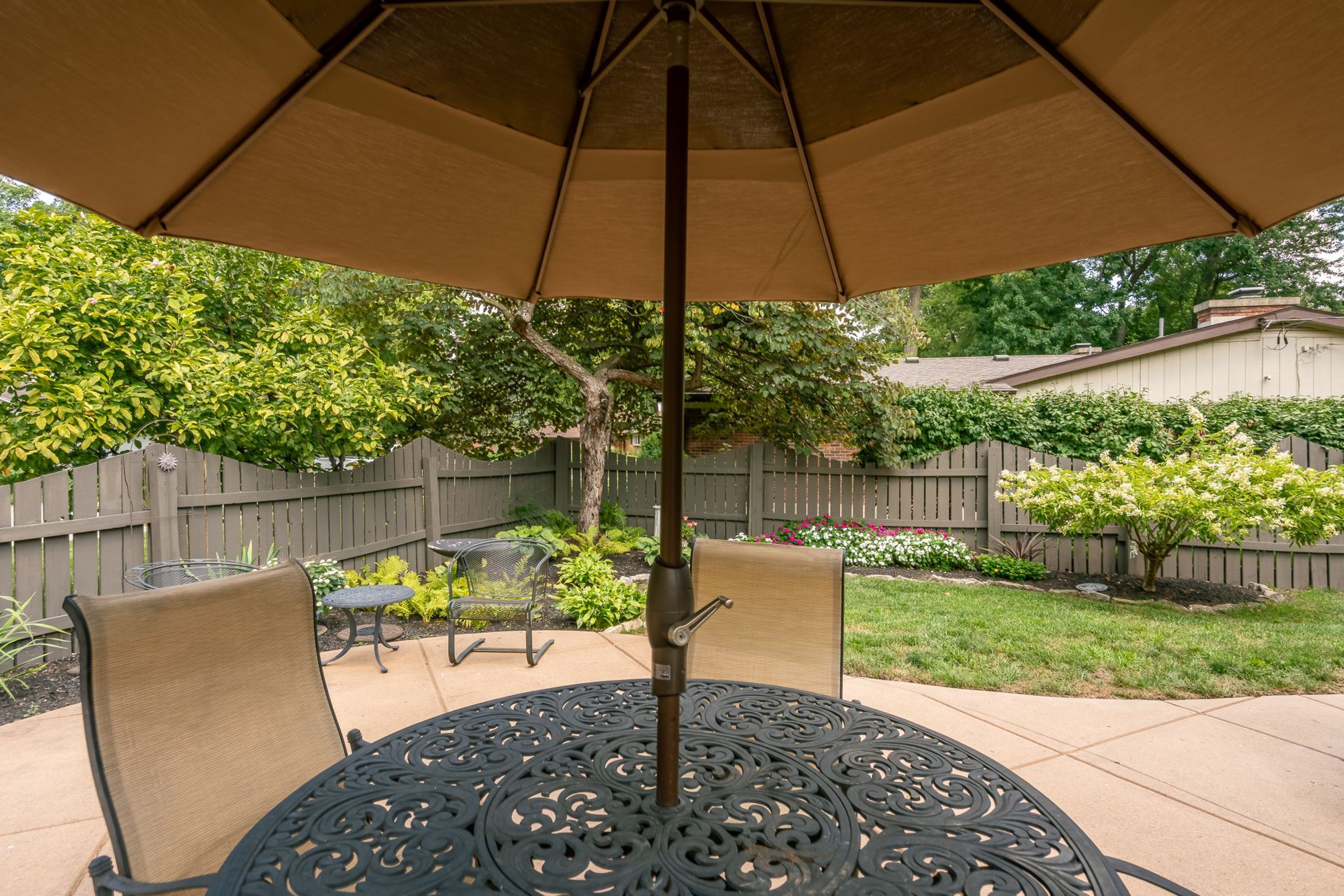 Patio table with umbrella, chairs, backyard, wooden fence, and greenery.
