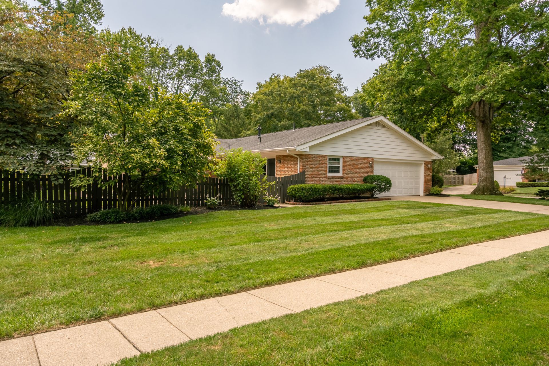 Brick house with green lawn, sidewalk, trees.