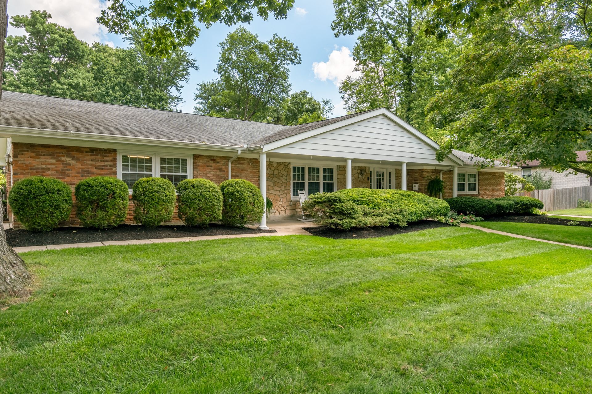 Brick ranch-style house with manicured lawn, shrubs, and trees on a sunny day.