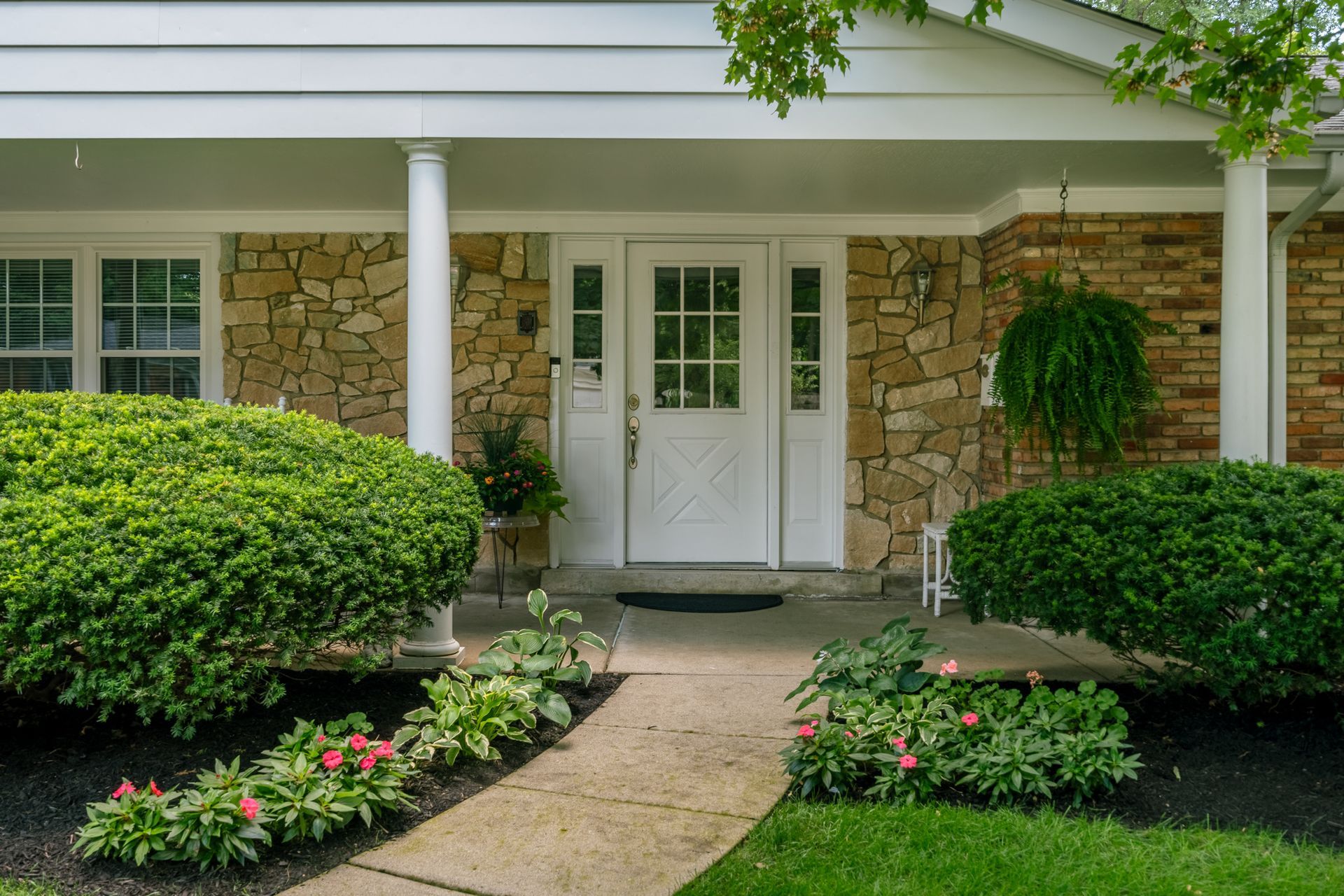 Stone facade entry with white door, porch, and landscaping.