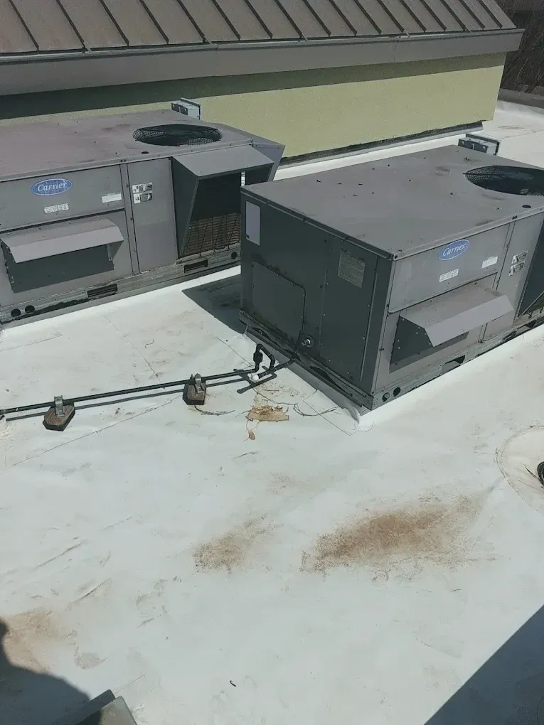 Two gray rooftop HVAC units on a white roof; brown stains and pipes visible.