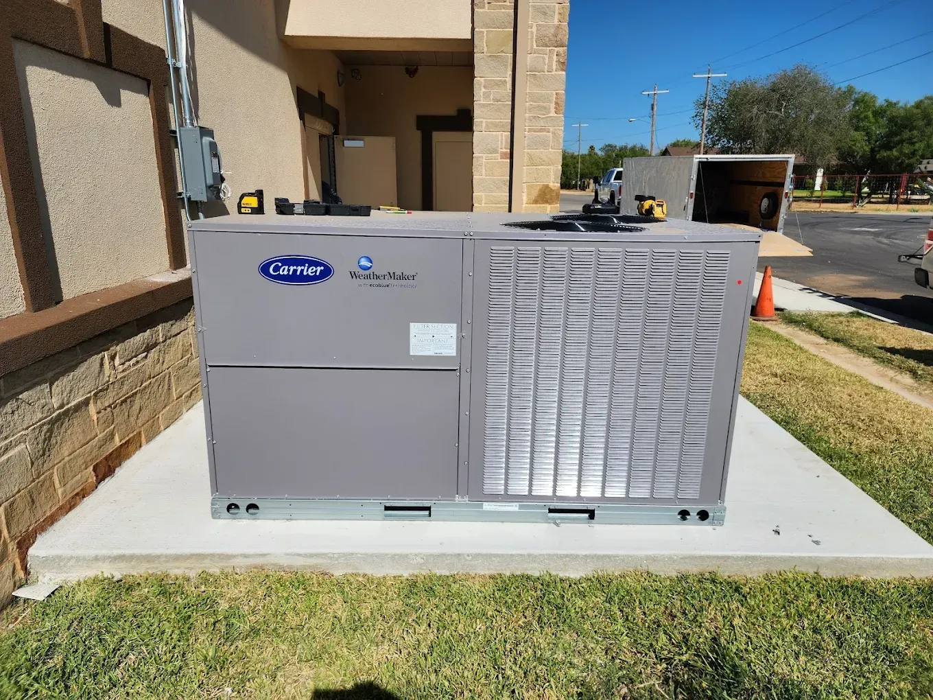 Gray Carrier HVAC unit on a concrete pad next to a building on a grassy area.