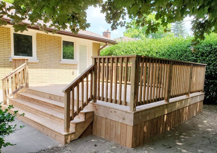 A wooden deck with stairs leading up to it is in front of a house.