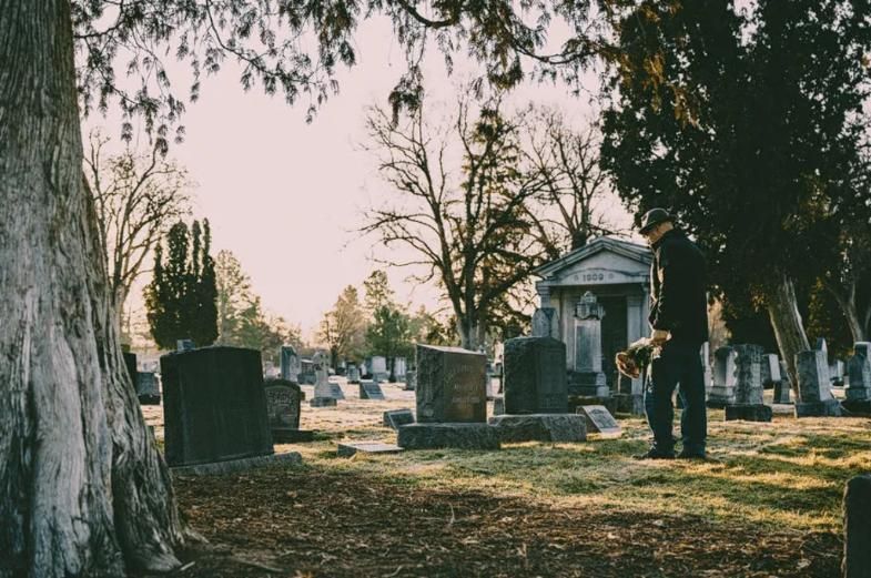 Man visiting a gravesite in a peaceful cemetery, reflecting the respectful memorial services offered by a funeral home and cremations in Canton Township, MI.