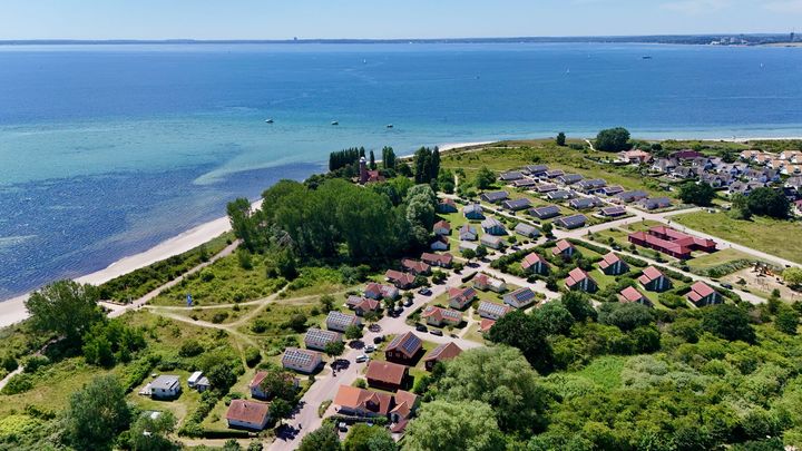 Blick auf ein Küstendorf mit Häusern, Strand und Meer unter blauem Himmel.