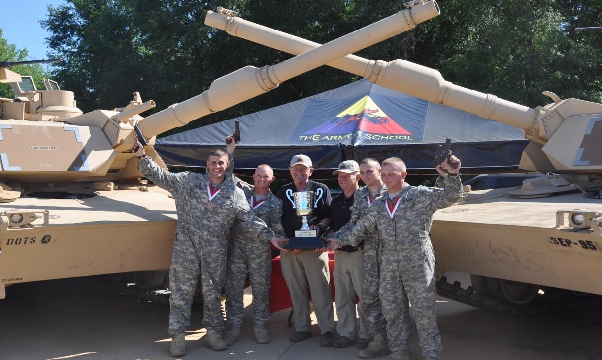 A group of soldiers holding a trophy in front of two tanks