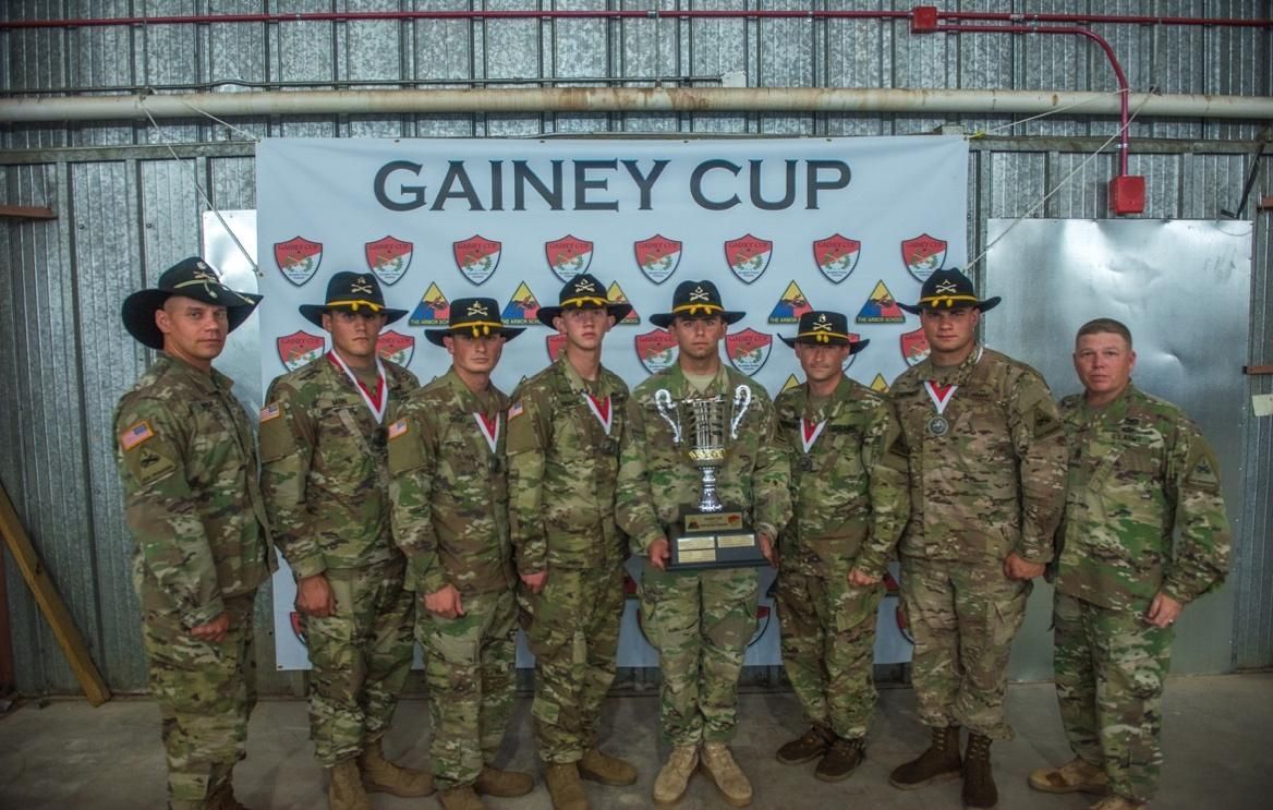 A group of soldiers are posing for a picture in front of a sign that says gainey cup.
