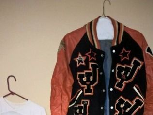 Varsity jacket with black body, orange sleeves, white shirt on a hanger.