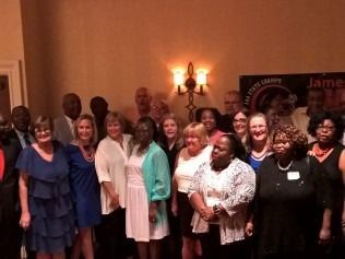 Group of people posing for a photo in a room with a wall sconce and a banner.